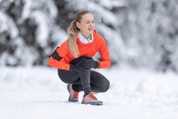 A young fit woman holds a reinforced knee after straining her cruciate ligament during cross-country training in the snow during the winter season.