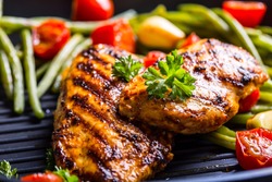 Grilled chicken breast in different variations with cherry tomatoes, green French beans, garlic, herbs, cut lemon on a teflon pan.