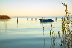 Calm lake with gentle waves, reeds and a decorative jetty with a blue boat