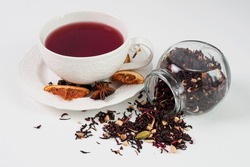 Leaf tea made from natural ingredients: black leaf, hibiscus, cardamom, dried orange. A spill of tea on the table. The concept of tea ceremony. Red tea in a cup. White background.