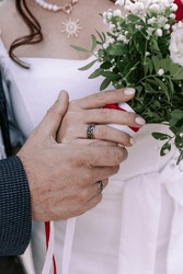 A vibrant vertical wedding photograph capturing a close-up of the bride and groom's hands, showcasing their wedding rings. In the background, a close-up of the bride and groom, as well as the bridal b
