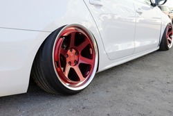 Tuned white car with extreme low suspension and red wheels.
