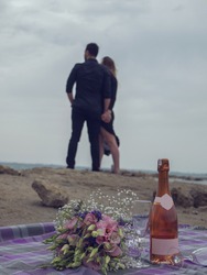Romantic picnic of loving couple with seaside and mountain view. expensive bottle of white wine, blank label and two glasses 