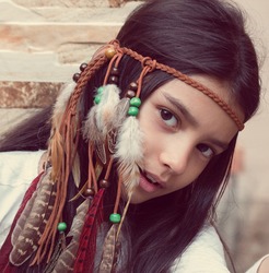 Little girl playing dress-up as Native American, wearing Indian headdress. Cute little girl playing in teepee.  Boho style.
