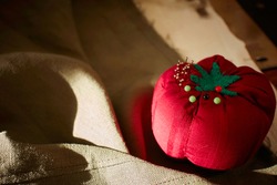 handmade imperfect tomato pincushion with glass head pins on natural colour linen fabric