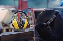 Yellow protective ear muffs hang on machines in heavy industrial plants. The concept is a PPE device that protects against loud noise in the operator's environment. industrial work safety equipment
