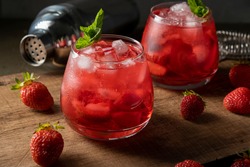 Red drink with strawberry, ice and mint. Refreshing summer cocktail in a glass on wooden table