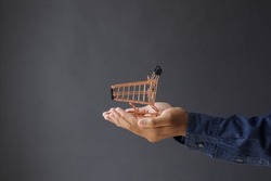 Close-up of consumer's hand giving mini shopping cart isolated on gray background