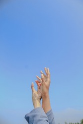 two pairs of hands of a girl wearing a blue sweater sticking out to the sky on a sunny day
