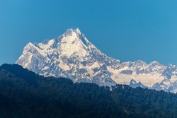 Kangchenjunga, also spelled Kanchenjunga, Kanchanjangha, and Khangchendzonga is the third highest mountain in the world. The snow clad peak of the mountain towering above the thick green forest.