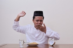 Sleepy Asian man in koko shirt or white muslim shirt and black cap  stretching yawning waking up and getting ready to eat pre dawn meal or muslim said suhoor at dawn before the sunrise