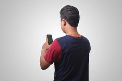 Back view portrait of Asian man wearing t-shirt, holding a mobile phone. Isolated image on white background