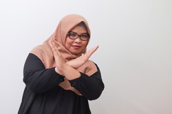 Portrait of serious Asian woman with hijab, showing X sign of hands for refusing an invitation from someone. Isolated image on white background