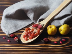 Berries  of the useful berberis plant, dry rose hips, viburnum in a wooden spoon and quince with a napkin on a dark on a wooden background, top view. Seasonal red barberry and yellow fruit for food