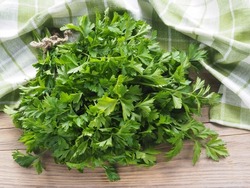 Fresh green parsley leaves with a napkin on a wooden table,  flat layout. Useful aromatic plant petroselinum crispum for use in cooking, herbal medicine and cosmetology
