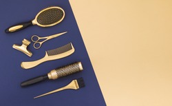 Hairdressing tools on a blue background and a yellow sheet with space for text. Gold hair salon accessories, comb, scissors, hair clip. 