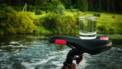 A glass of drinking water on the saddle of a sports bike, water in a transparent glass against the backdrop of a forest with a river