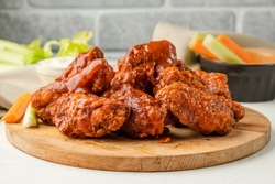 Appetizing fried buffalo chicken wings served on a wooden board with vegetables on the background.