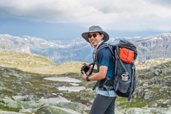 Young Asian man traveller with backpack taking picture while trekking in Trolltunga mountain cliff, famous trekking route in Odda, Norway, Scandinavia, Europe