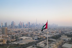 Unique view of UAE, United Arab Emirates national flag waving in the air with Dubai skyline in background during sunset