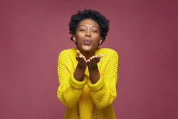 Positive african american young woman with curly afro hair blowing kiss farewell gesture, feeling love and gratefulness