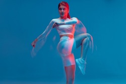 Fitness girl rasing hips, doing warm up exercise for legs on blue backdrop. Long exposure, motion blur. Sports workout