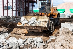 A front-end loader at a construction site removes debris from reinforced concrete. Collection and removal of detached building materials. Selective focus