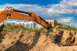 An excavator digs a foundation pit for the construction of a residential building. New residential buildings in the background. Construction production. Excavation