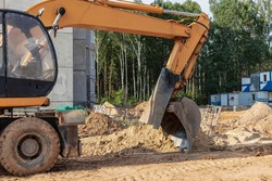 An excavator digs a foundation pit for the construction of a residential building. New residential buildings in the background. Construction production. Excavation