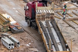 A large truck delivers material to the construction site. Supply of metal fittings for the construction of a monolithic reinforced concrete house. Acceptance of building materials