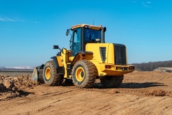 Bulldozer or loader moves the earth at the construction site against the blue sky. An earthmoving machine is leveling the site. Construction heavy equipment for earthworks