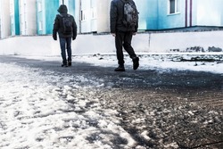 People walk on a slippery road made of melted ice. View of the legs of a man walking on an icy pavement. Winter road in the city. Injury after a fall on an icy road