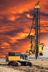 Hydraulic drilling machine at the construction site makes piles. Pile field. Modern drilling rig. Piles against the sunset. Work drilling rig in difficult conditions