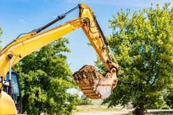 An excavator digs a pond pit in the garden against the blue sky. Digging a pit with an excavator. Earthmoving equipment and earthworks