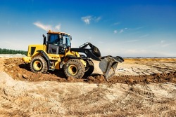 Powerful bulldozer or loader moves the earth at the construction site against the sky. An earthmoving machine is leveling the site. Construction heavy equipment for earthworks