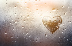Heart painted on glass in Rainy weather, is fogged up and there are many drops on it, in a romantic pink tint, sunny sunset