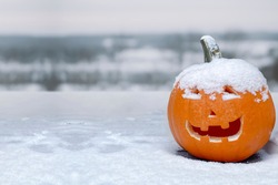 A jack-o'-lantern carved pumpkin during a snow fall during the fall. Concept: cold halloween. Snow fall during halloween