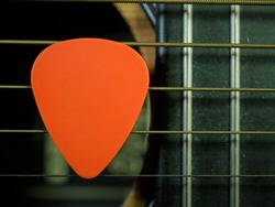 Close up of pick plectrum on acoustic guitar showing strings and fret board