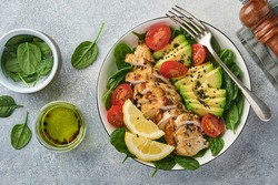 Fresh green salad with grilled chicken fillet, spinach, tomatoes, avocado, lemon and black sesame seeds with olive oil in white bowl on light slate background. Diet Concept. Top view copy space