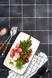 Asparagus, mushrooms, mozzarella cheese, grilled radish and cress salad, oil olive salad on rectangular ceramic plate on black old tile table background. Healthy diet grilled food concept. Top view.