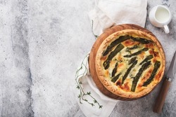 Quiche. Homemade asparagus pie or quiche with cheese, pecorino, bacon and spinach on gray concrete light table background. Asparagus and cheese tart.  French Quiche. Top view.