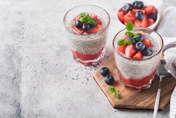 Chia strawberry pudding. Healthy vegan breakfast chia seeds pudding with fresh berries and mint in glass on gray concrete background. Concept of healthy eating, dieting, fitness menu. Selective focus.