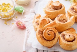 Easter breakfast Holliday concept. Easter bunny buns rolls with cinnamon made from yeast dough with orange glaze, easter decorations, colored eggs on pink spring background. Easter Holliday card.