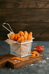 French fries in metal wire basket with salt and ketchup on old wooden dark background clous up. Fried potatoes. Fast food and unhealthy food concept. 