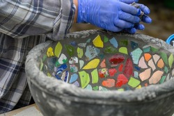 People decorate earthenware with mosaic techniques in the master class or in the fresh air in the workshop. Homemade mosaic flower pot with porcelain pieces.