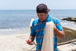 Latino fisherman checking his cell phone on the beach