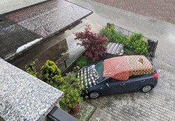 Car covered in blankets during strong hail storm. Car protection against hail during stormy weather