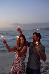 happy couple holding sparklers celebrating new years eve on beach at sunset with sparkle firework