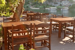 Wooden empty tables with massive chairs in restaurant on river bank. Horizontal photo.