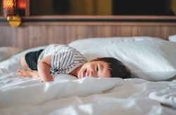 Portrait of Little boy wear striped shirt feel relax and laydown on the bed, looking at camera. A caucasian kid feel comfortable lying down on the bed with smiling face. Bed Vibes concept. Happy Kids.